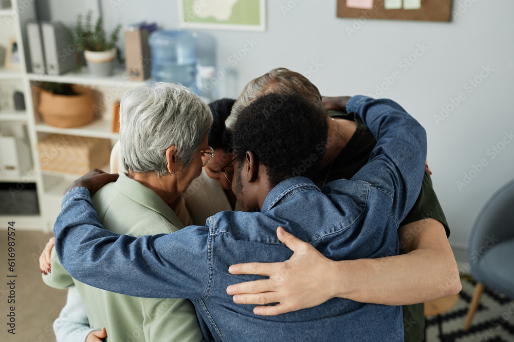 Group of intercultural people in casualwear standing in embrace in circle in front of camera while supporting each other during psychological session Group of intercultural people in casualwear standing in embrace in circle in front of camera while supporting each other during psychological session