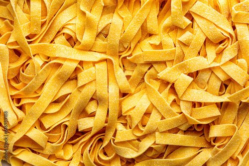 Homemade fresh, uncooked tagliatelle or fettuccine background,  is a traditional type of italian pasta.  Long, flat ribbons traditionally made of egg and flour. Directly above.