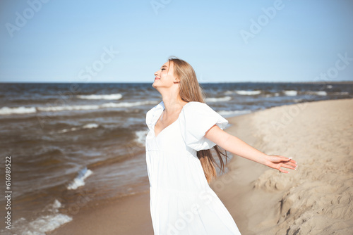 Happy smiling beautiful woman is on the ocean beach in a white summer dress  open arms