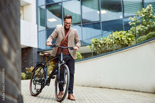 Fotografie A happy businessman pushing a bicycle in front of the company and going home