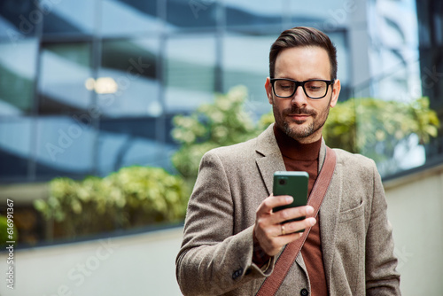 Obraz na płótnie A successful businessman with glasses on using a mobile phone outside the company. w salonie