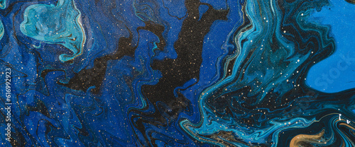 Fluid art background in blue tints with gilding. Flowing wave effect of liquid ink. Dark phantom blue with golden stains. Fantasy abstract texture of acrylic paints. Surreal color mix. Gold on blue.