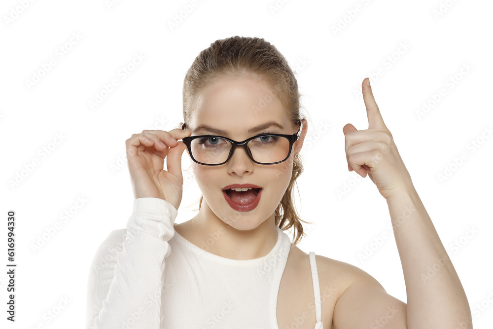 Portrait of beautiful positive blonde woman wearing glasses and pointing up on a white background