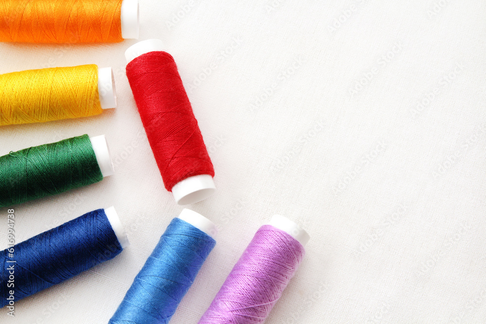 Spool of sewing threads multicolored on white cotton fabric with copy space for design art work. Spool of sewing threads multicolored on white cotton fabric with copy space for design art work.