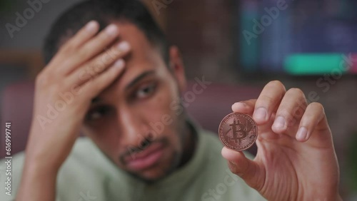 Bitcoin falling. Cryptocurrency market crash, downgrade of electronic currency. Dissapointed trader holding bitcoin with stock market graphs on background. Bitcoin downtrend. Crisis of cryptocurrency.