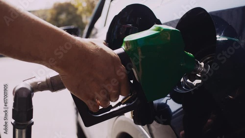 Backlit close up of Latino man pumping gas into Toyota Prius at Gas Station on a sunny day.