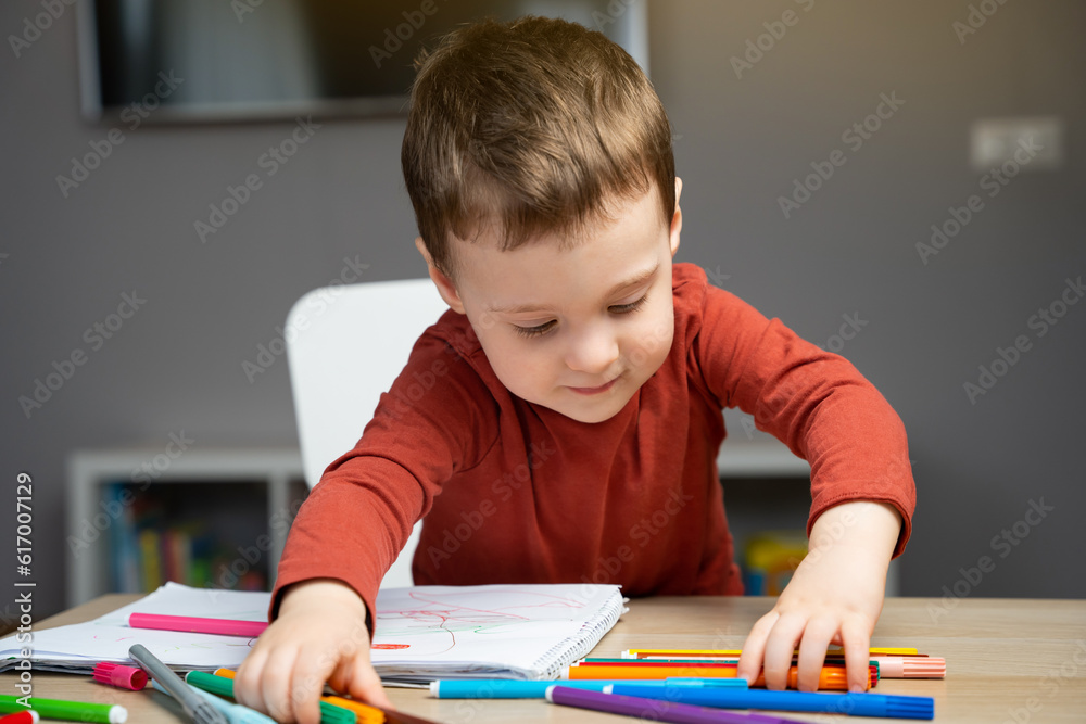 A cute happy little toddler boy of two years playing with markers in the album in the children's room at home. Educational activities for kids. Selective focus. A cute happy little toddler boy of two years playing with markers in the album in the children's room at home. Educational activities for kids. Selective focus.