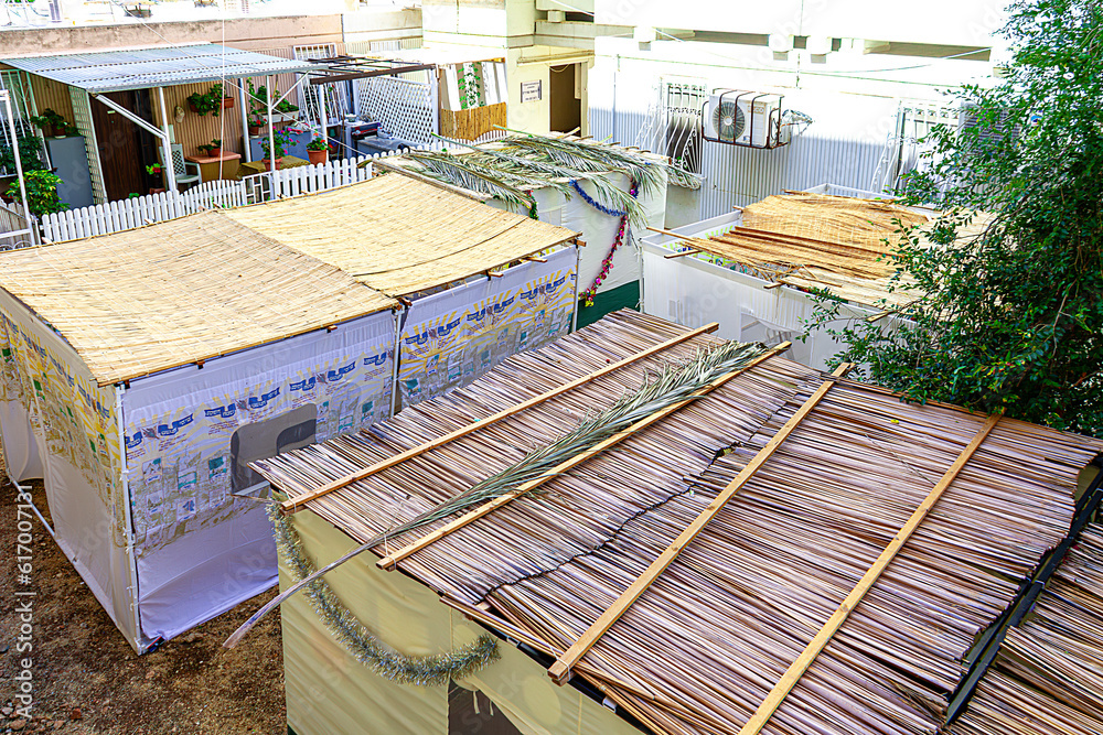 Four sukkahs outside in a street with a garden and trees near a building, a traditional building for the Jewish holiday of Sukkot. Jewish tradition. Four sukkahs outside in a street with a garden and trees near a building, a traditional building for the Jewish holiday of Sukkot. Jewish tradition.