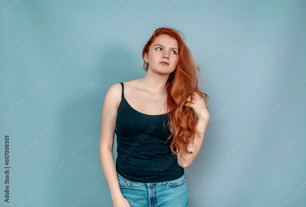 Dreamy red-haired woman. Black T-shirt and blue jeans. Looks to the side. Hand near hair.. Dreamy red-haired woman. Black T-shirt and blue jeans. Looks to the side. Hand near hair..