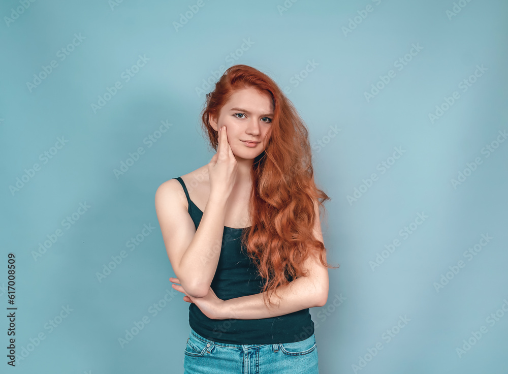 Dreamy woman with long red hair in a black tank top on a gray background. Hand near face. Dreamy woman with long red hair in a black tank top on a gray background. Hand near face.