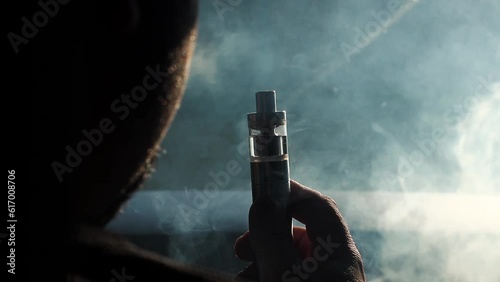 Young vaper man with beard vaping mechanical mod. Guy smokes an electronic cigarette by blowing a smoke vapor. Holds in hand Sitting at the wheel of a car. Space for text