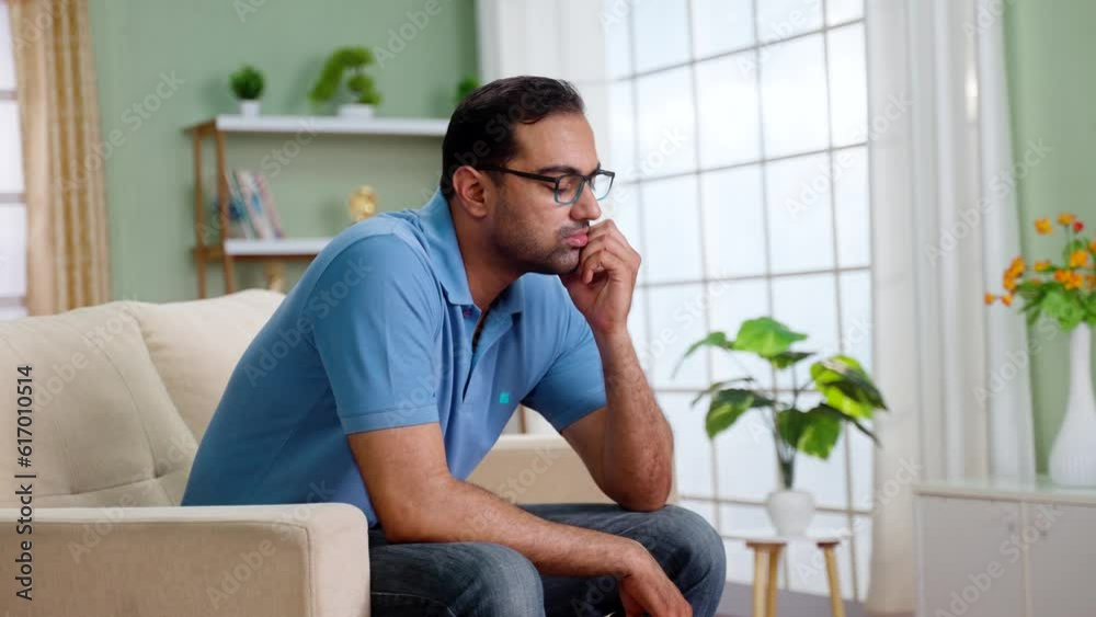Worried indian man in deep thinking while sitting on sofa at home - concept of financial problem, love breakup and mental illness. Worried indian man in deep thinking while sitting on sofa at home - concept of financial problem, love breakup and mental illness.