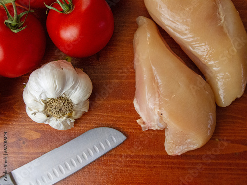 Meal preparation. Boneless, skinless chicken breasts, fresh tomatoes, and garlic. Chef's knife. Healthy eating.