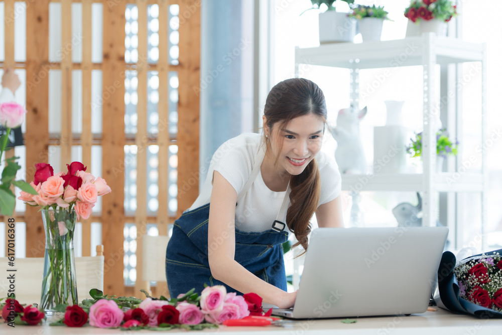 Young asian woman florist working with laptop in flower shop
