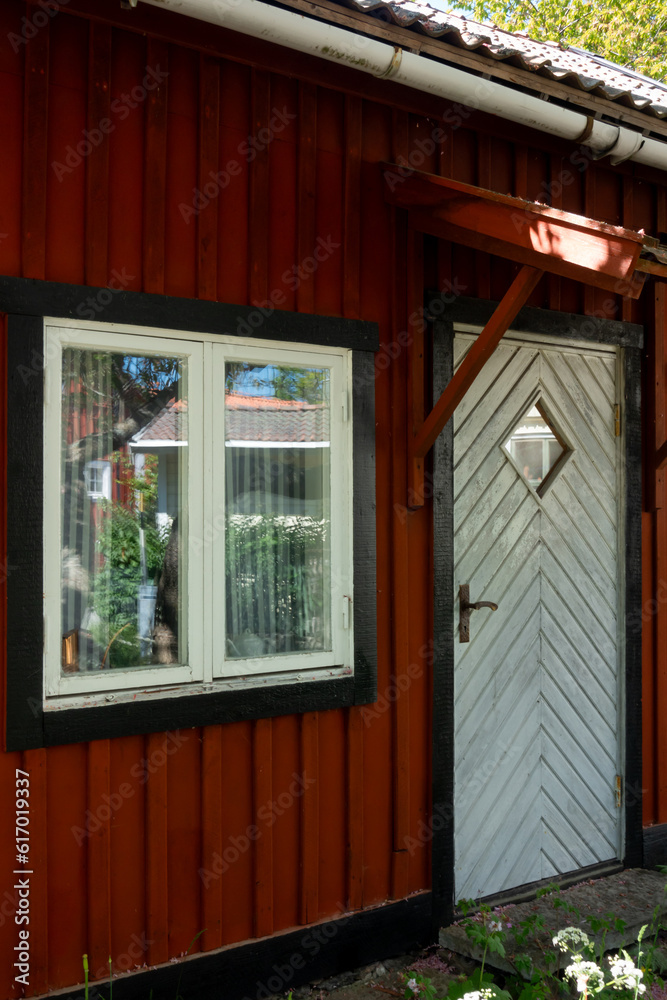 White door entrance to a falu red paint cottage in the forest in Swedish for a cabin escape concept and warm Swedish summer vacation White door entrance to a falu red paint cottage in the forest in Swedish for a cabin escape concept and warm Swedish summer vacation