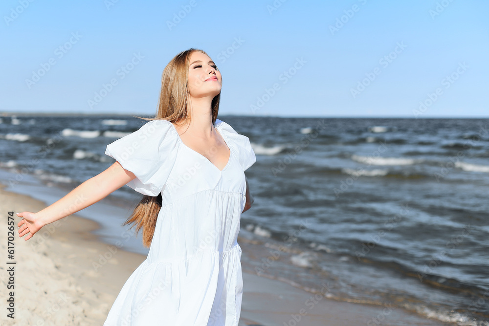 Happy smiling beautiful woman is on the ocean beach in a white summer dress, open arms Happy smiling beautiful woman is on the ocean beach in a white summer dress, open arms