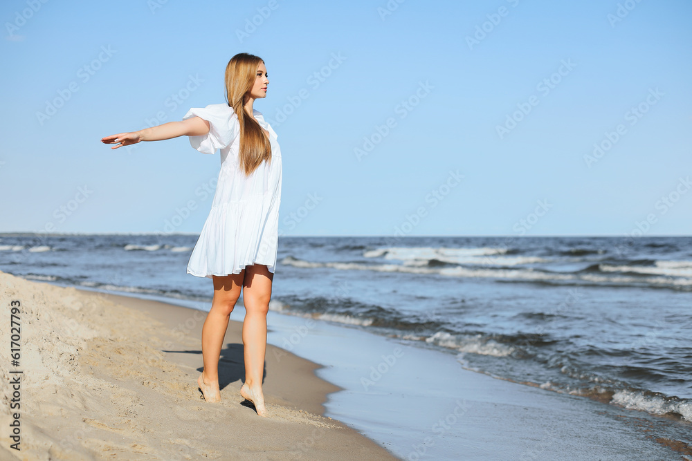 Happy smiling beautiful woman is walking on the ocean beach with open arms