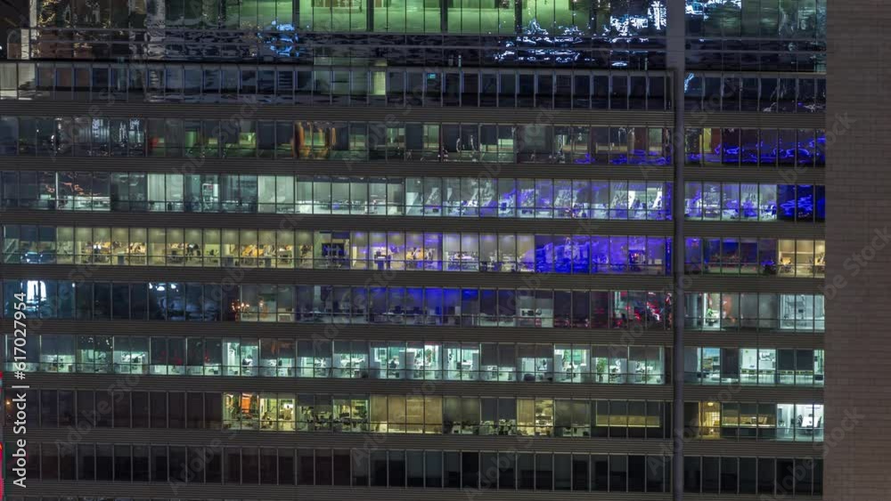 Frontal view of night facade of business tower building with a lot of windows with light timelapse. Life in every window. Aerial view of the glass facade of an office skyscraper.