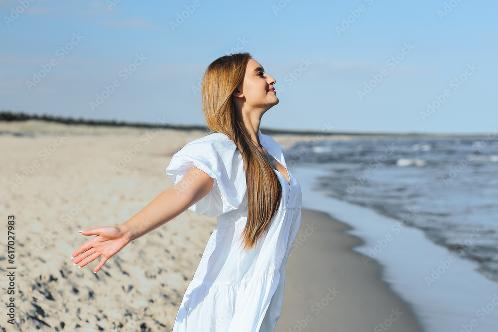 Happy smiling beautiful woman is on the ocean beach in a white summer dress, open arms Happy smiling beautiful woman is on the ocean beach in a white summer dress, open arms