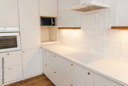 Modern kitchen interior. Stylish white kitchen cabinets with brass knobs  granite counter  wooden shelves with light and appliances in new scandinavian house. Modern minimal kitchen design
