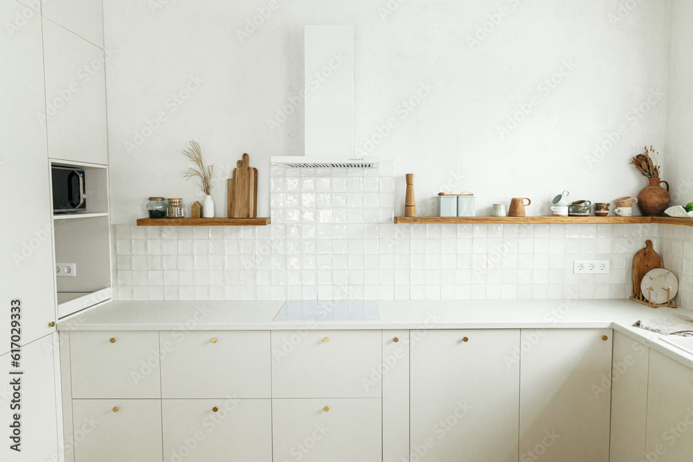 Modern minimal kitchen design. Stylish white kitchen cabinets with brass knobs, granite island, appliances and utensils on wooden shelves in new scandinavian house. Modern kitchen interior.