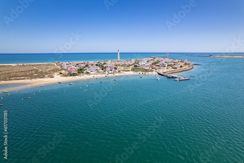 Aerial seascape view of Cape Santa Maria lighthouse island, Praia do Farol beach, one of the barrier islands that protect the Ria Formosa natural park, in Algarve Tourism Destination region, Portugal