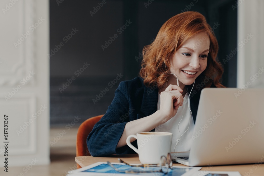 Happy female entrepreneur has online conference, uses laptop with wireless internet and earphones at home or coworking space. Happy female entrepreneur has online conference, uses laptop with wireless internet and earphones at home or coworking space.