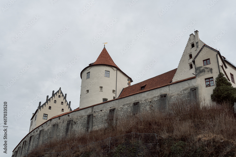 A small white castle in the old town of Füssen photographs in winter with light snow and a park in the foreground