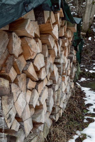 A supply of tree trunks have been stacked and is located on the side of the path and is with a tarpaulin