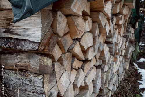 A supply of tree trunks have been stacked and is located on the side of the path and is with a tarpaulin