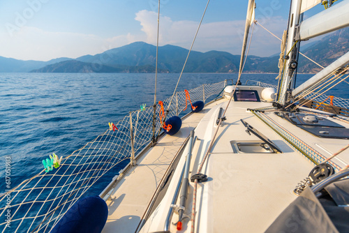 Yacht sailing in an open sea. Close-up view of the deck, mast and sails. Clear sky, waves and water splashes