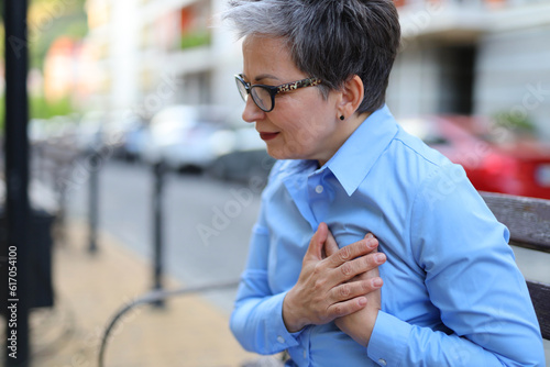 The emotion of pain in a woman clutching her heart with her hands while sitting on a street bench. Heart attack concept.