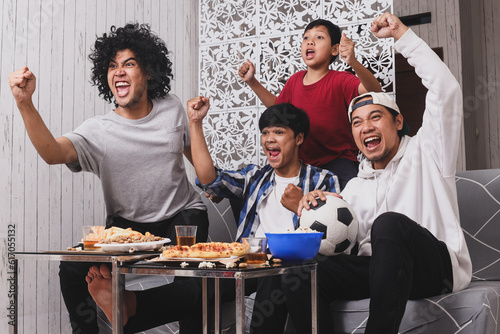 Fotografía Happy friends, family or football fans watching soccer on tv raising hands with happy faces celebrating victory at home