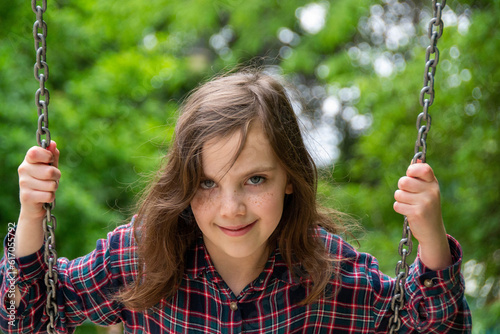 Close up happy little child girl play and sitting on the swing in the nature park. Teen girl on a swing in the summer park. High quality photo