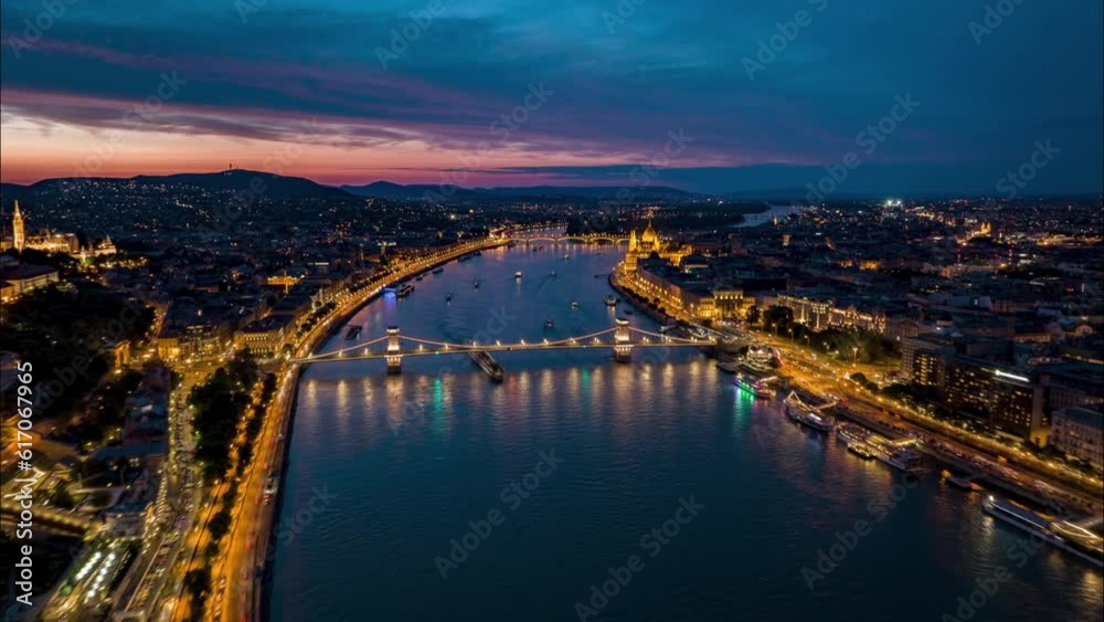 Forward fly above wide river flowing through capital. Aerial panoramic hyperlapse shot of illuminated landmarks and streets around Danube river in city. Budapest, Hungary Forward fly above wide river flowing through capital. Aerial panoramic hyperlapse shot of illuminated landmarks and streets around Danube river in city. Budapest, Hungary