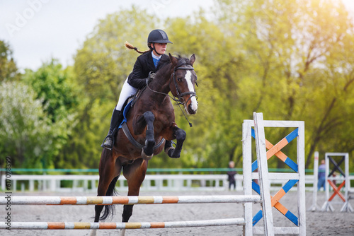 Young woman riding horseback jumping over the hurdle on showjumping course in equestrian sports event © skumer