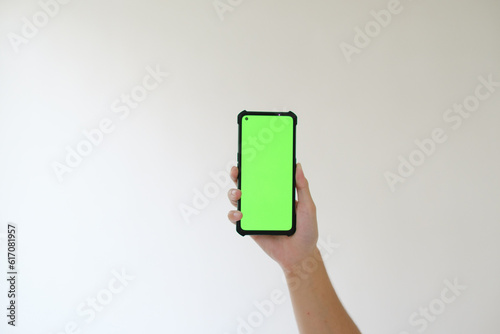 A hand is lifting up a smartphone with a green screen. Isolated white background. Suitable for advertisement.