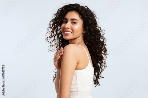 A model girl with glowing skin and thick black and curly hair looks over her shoulder at the camera against a blue background