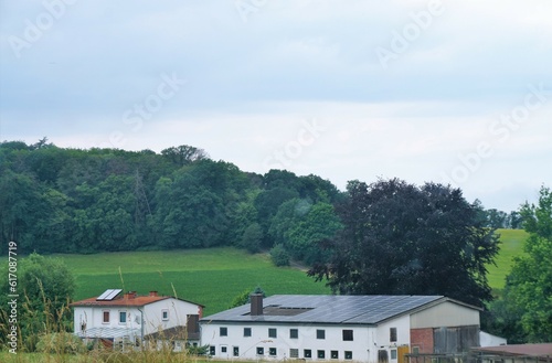 Grüne Landschaft Panorama mit Bauernhof vor Berghügel mit grünen Feldern und Wald vor Himmel bei Sonne am Mittag im Sommer