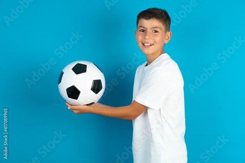 Little hispanic boy wearing white T-shirt holding a football ball pointing aside with hands open palms showing copy space  presenting advertisement smiling excited happy