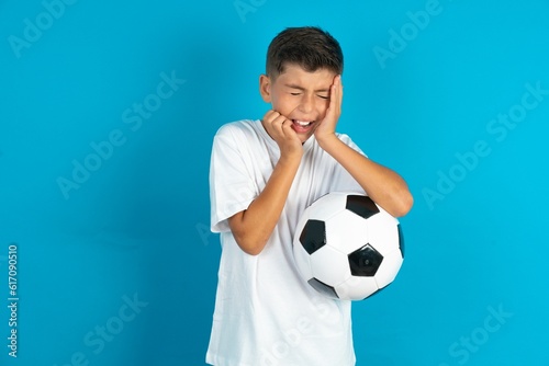 Doleful desperate crying Little hispanic boy wearing white T-shirt holding a football ball , looks stressfully, frowns face, feels lonely and anxious © Jihan
