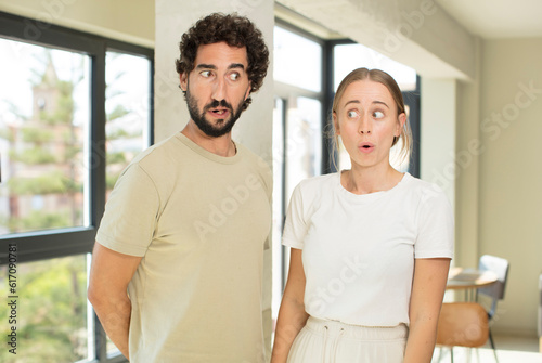 young adult couple feeling shocked and surprised, looking to copy space on the side with amazed, open-mouthed look