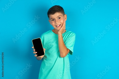 Little hispanic boy wearing green T-shirt hold hand modern technology use touch face palm astonished impressed scream wow omg unbelievable unexpected