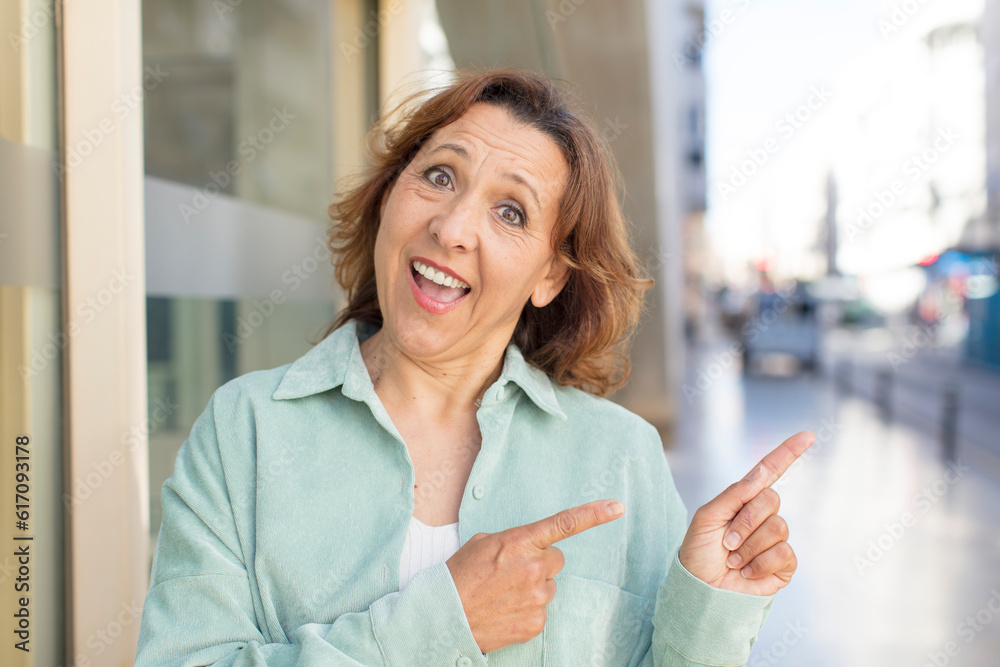 Fototapeta premium middle age woman smiling cheerfully and pointing to copy space on palm on the side, showing or advertising an object