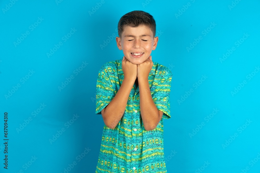 Cheerful Little hispanic boy wearing green aztec shirt has shy satisfied expression, smiles broadly, shows white teeth, People emotions Cheerful Little hispanic boy wearing green aztec shirt has shy satisfied expression, smiles broadly, shows white teeth, People emotions