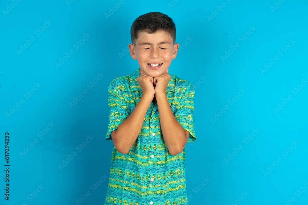Little hispanic boy wearing green aztec shirt grins joyfully, imagines something pleasant, copy space. Pleasant emotions concept. Little hispanic boy wearing green aztec shirt grins joyfully, imagines something pleasant, copy space. Pleasant emotions concept.