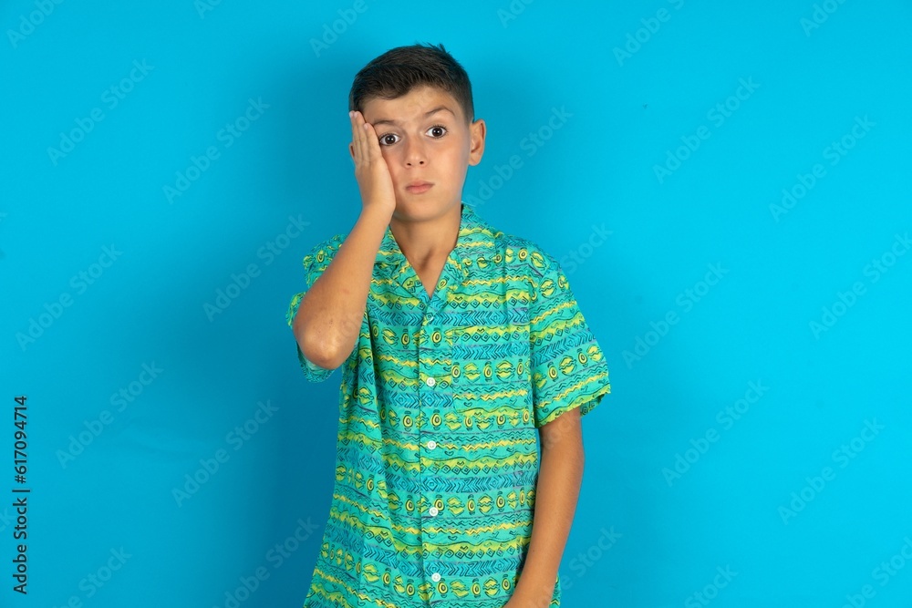 Little hispanic boy wearing green aztec shirt with sad expression covering face with hands while crying. Depression concept. Little hispanic boy wearing green aztec shirt with sad expression covering face with hands while crying. Depression concept.