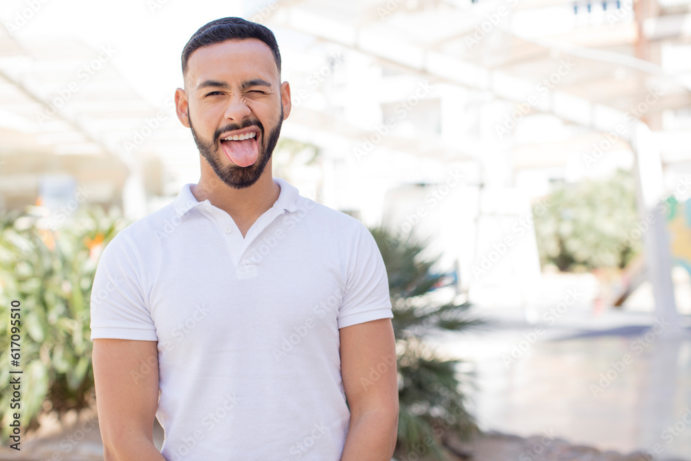 young handsome man with cheerful, carefree, rebellious attitude, joking and sticking tongue out, having fun