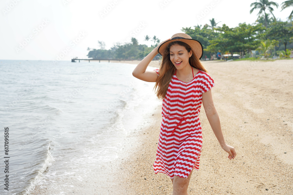 Pretty girl plays with water on empty tropical beach. Beautiful young woman having fun on sand beach. Escape travel concept.