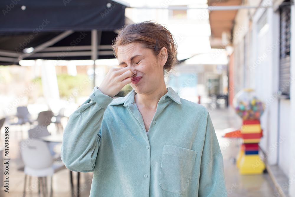 pretty young woman feeling disgusted, holding nose to avoid smelling a foul and unpleasant stench pretty young woman feeling disgusted, holding nose to avoid smelling a foul and unpleasant stench